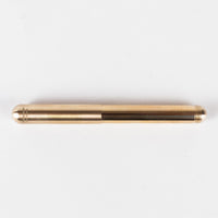 Closed sleek round brass pen with engraved logo and screw thread at one end on grey background