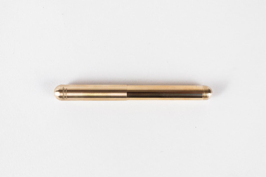 Closed sleek round brass pen with engraved logo and screw thread at one end on grey background