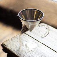 Glass carafe with stainless steel coffee filter on wooden bench in shop