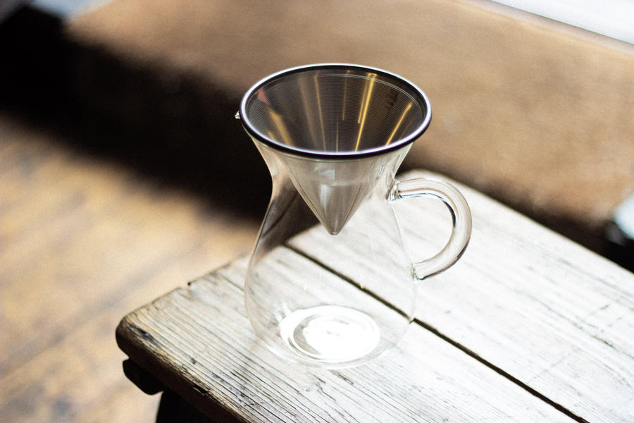 Glass carafe with stainless steel coffee filter on wooden bench in shop