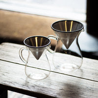 Two glass carafes with stainless steel coffee filters on wooden bench in shop
