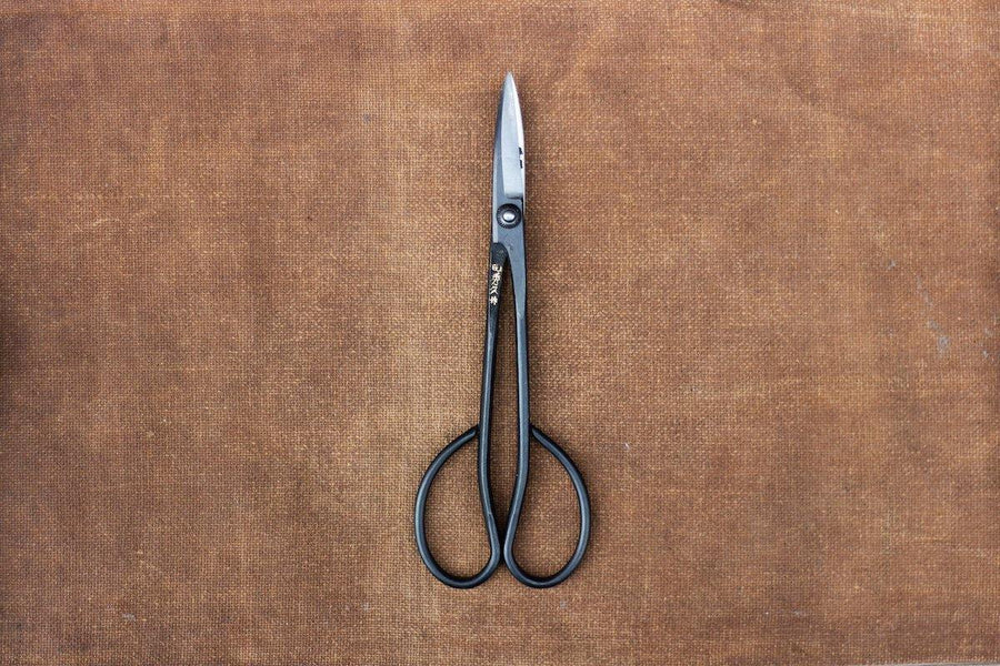 Long handled metal scissors with engraved Japanese characters on brown cloth